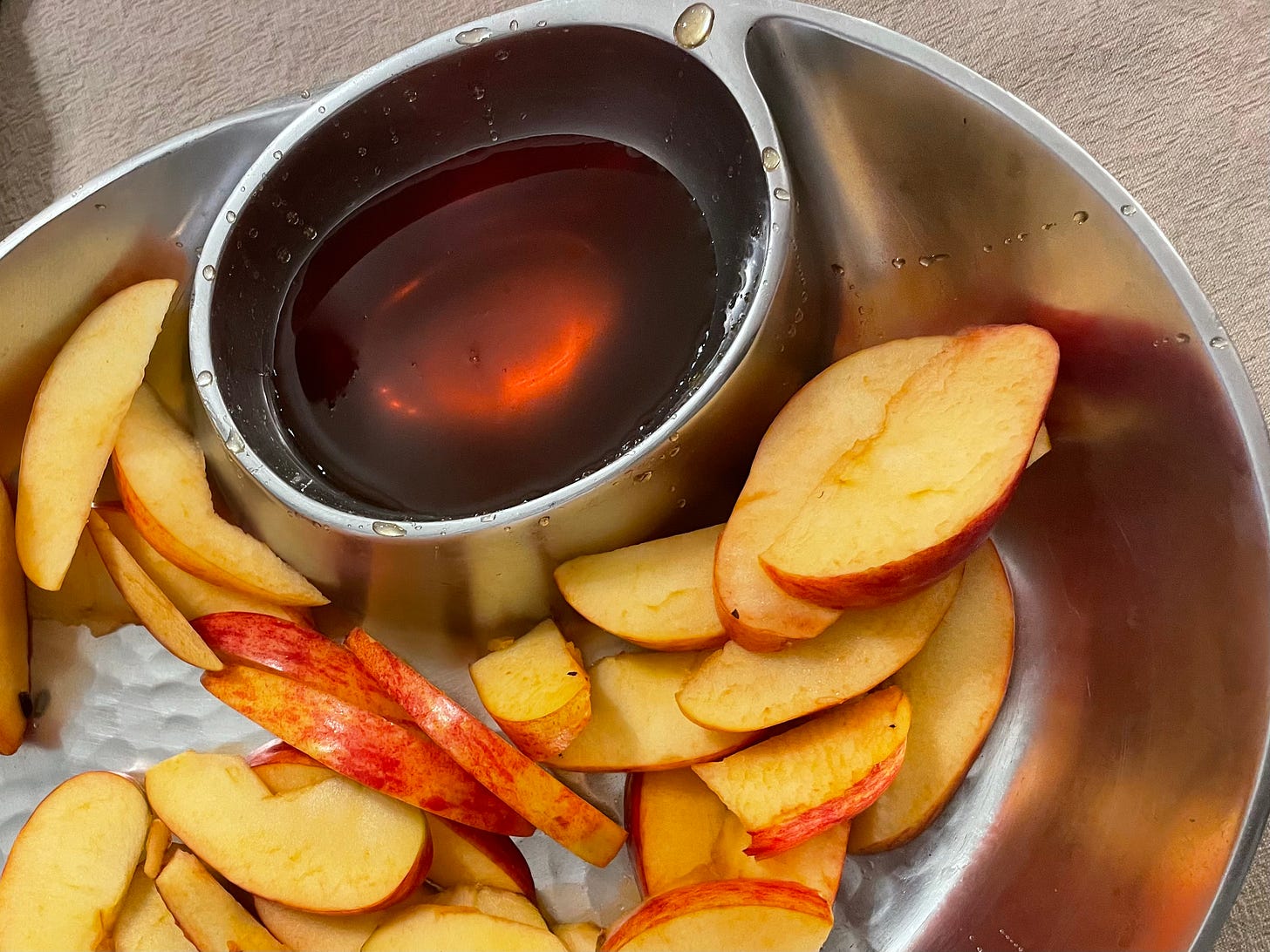 Some apple slices in a stainless steel tray with a small bowl of brown honey.