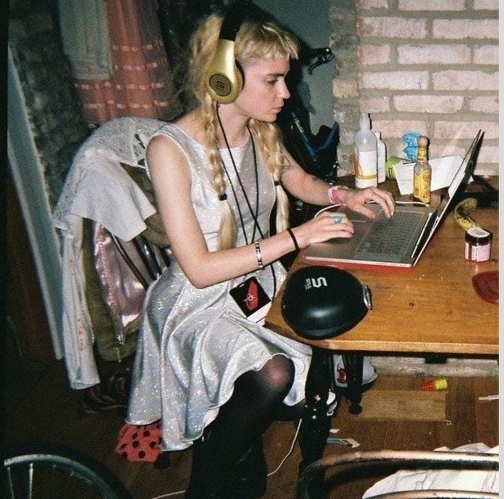 This may contain: a woman sitting at a table using a laptop computer with headphones on her ears