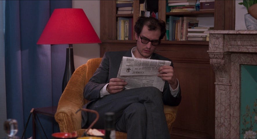 A man sitting in a chair, reading a newspaper intently.