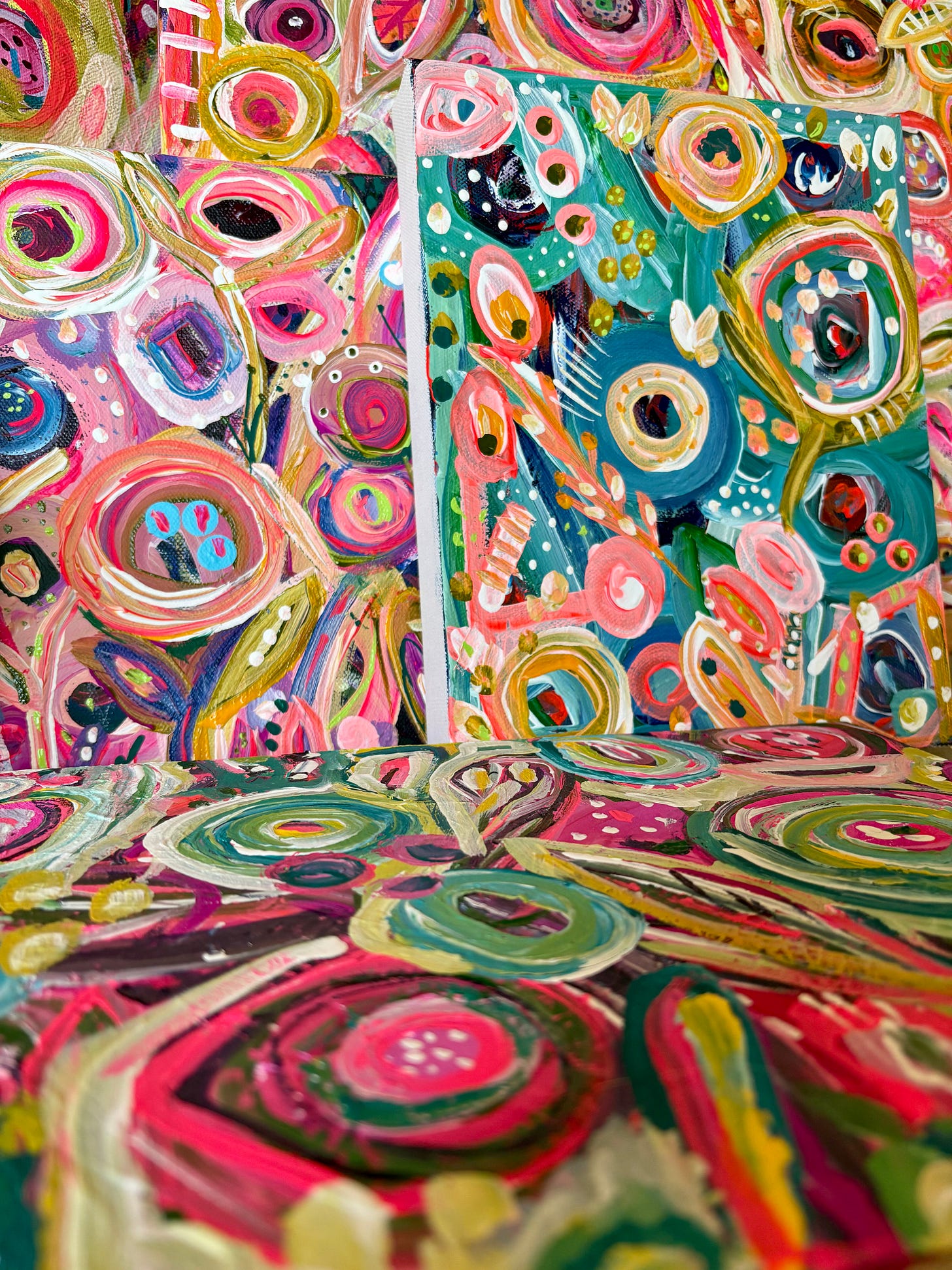 Close-up photo of several abstract paintings in progress by Kelly Kingman, featuring vivid swirls of teal, magenta, pink, yellow, and green. The canvases overlap, showing layered brushstrokes, circular forms, and energetic patterns that evoke both chaos and renewal. Close-up photo of several abstract paintings in progress by Kelly Kingman, featuring vivid swirls of teal, magenta, pink, yellow, and green. The canvases overlap, showing layered brushstrokes, circular forms, and energetic patterns that evoke both chaos and renewal.