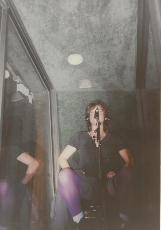 Woman in a recording booth singing into a mic. She has purple tights on and short hair Woman in a recording booth singing into a mic. She has purple tights on and short hair