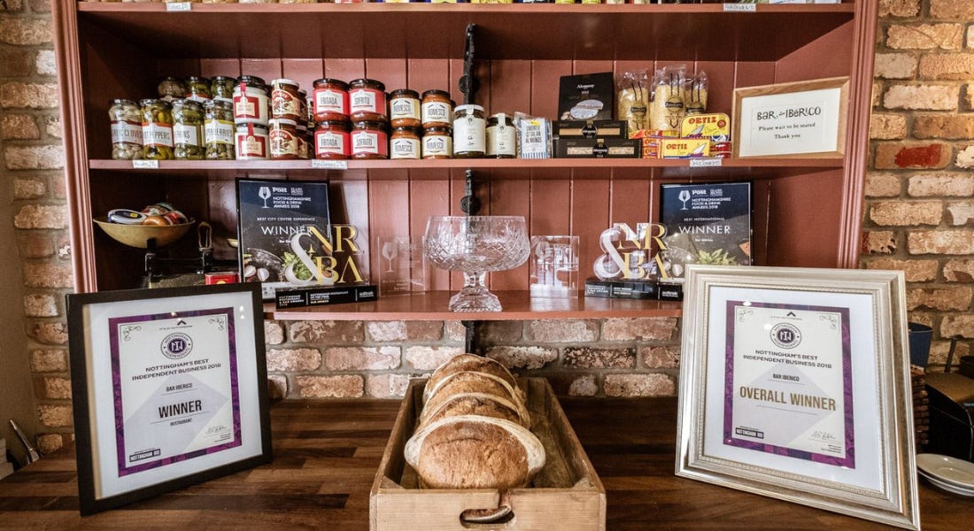 A restaurant desk with jars of food and awards on a shelf, and two certificates and a board of bread in front of it A restaurant desk with jars of food and awards on a shelf, and two certificates and a board of bread in front of it