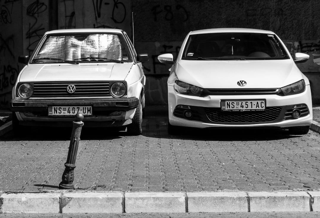 grayscale photo of two Volkswagen cars parked on sidewalk grayscale photo of two Volkswagen cars parked on sidewalk