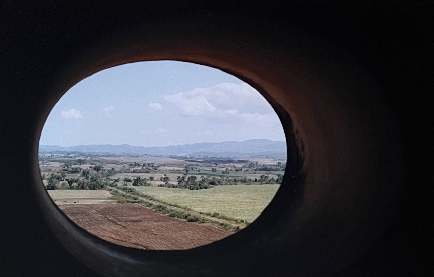Colour photo of fertile fields captured through an oval hole in some kind of concrete or similar structure.