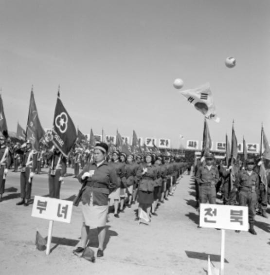 Black-and-white photo of the April 1, 1968 ceremony launching South Korea’s Homeland Reserve Forces in Daejeon: uniformed ranks parade with unit flags, the Taegeukgi flies overhead, and placards read “부녀” (women) and “전북” (North Jeolla) at the front.