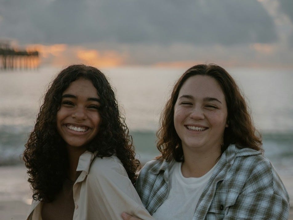 two women sitting on the beach smiling for the camera two women sitting on the beach smiling for the camera