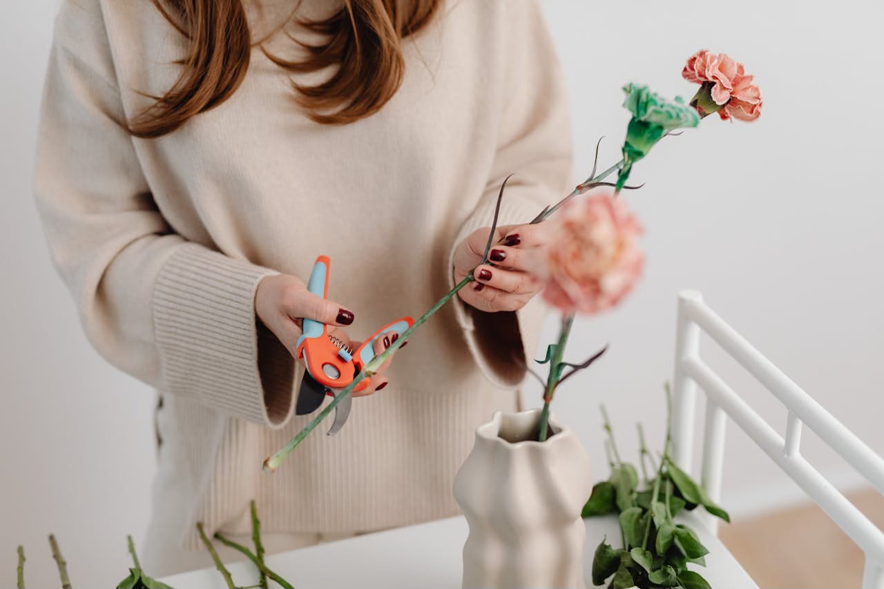 Cropped image of a woman with red hair wearing a beige sweater twimming and arranging flowers