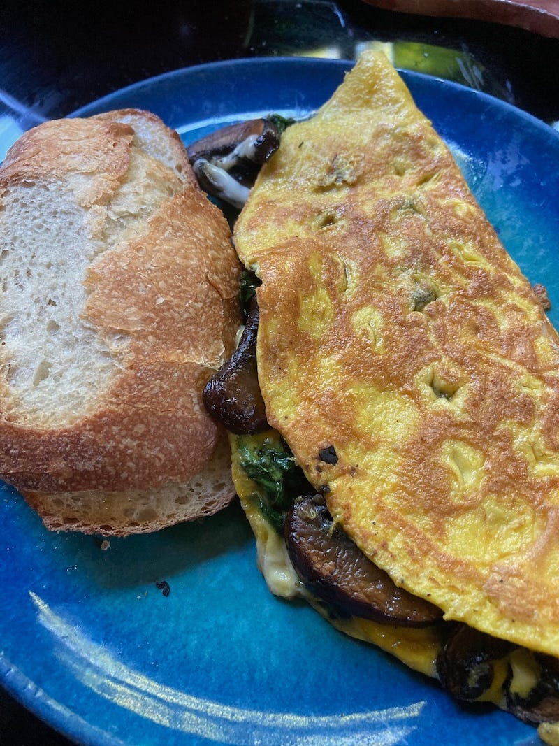 A blue plate with a mushroom and spinach omelette and some crusty bread. A blue plate with a mushroom and spinach omelette and some crusty bread.