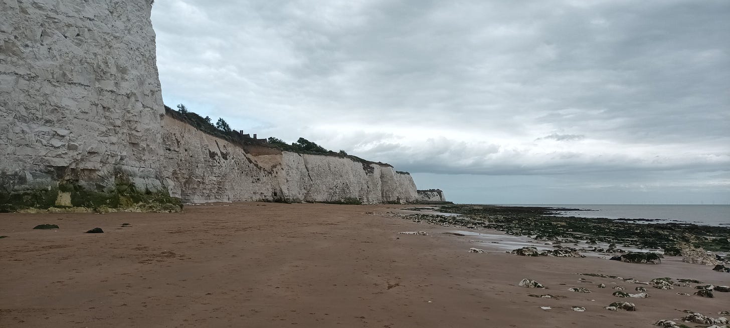 Chalk cliffs showing signs of erosion and the sandy beach below, grey skies and sea in the distance