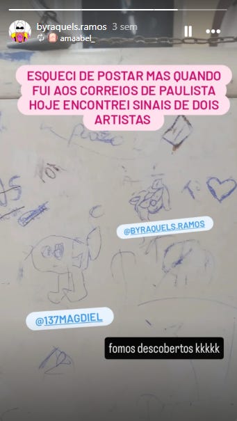 A imagem consiste em um print de tela de um story do Instagram, apresentado no formato vertical com barras pretas nas laterais. A foto de fundo captura o que parece ser uma mesa ou balcão branco de atendimento público, visivelmente desgastado e coberto por diversos rabiscos, corações e assinaturas feitos com caneta esferográfica azul. Centralizado na parte superior, há um bloco de texto destacado com fundo rosa e letras brancas que diz "ESQUECI DE POSTAR MAS QUANDO FUI AOS CORREIOS DE PAULISTA HOJE ENCONTREI SINAIS DE DOIS ARTISTAS". Logo abaixo, duas etiquetas azuis de marcação do Instagram identificam os autores dos desenhos na mesa: a tag @BYRAQUELS.RAMOS aponta para o contorno de um rosto minimalista, enquanto a tag @137MAGDIEL indica a ilustração de um personagem cabeçudo com olhos grandes. Bem na parte inferior da tela, uma pequena caixa de texto preta traz a legenda "fomos descobertos kkkkk", reagindo ao achado com bom humor. Por fim, no canto superior esquerdo, a interface da rede social revela a foto de perfil e o nome do usuário @byraquels.ramos, acompanhado da indicação de que a postagem foi feita há três semanas.