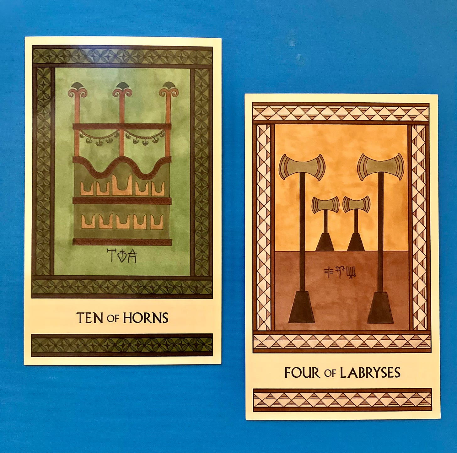 Two Minoan Tarot cards side by side on a bright blue surface. The Ten of Horns is in shades of green and brown. It shows an ikrion, a fancy platform found on Minoan ships, for special passengers to ride in. The Four of Labryses is in shades of gold, cream, and tan. It shows four labryses standing in a quiet room.