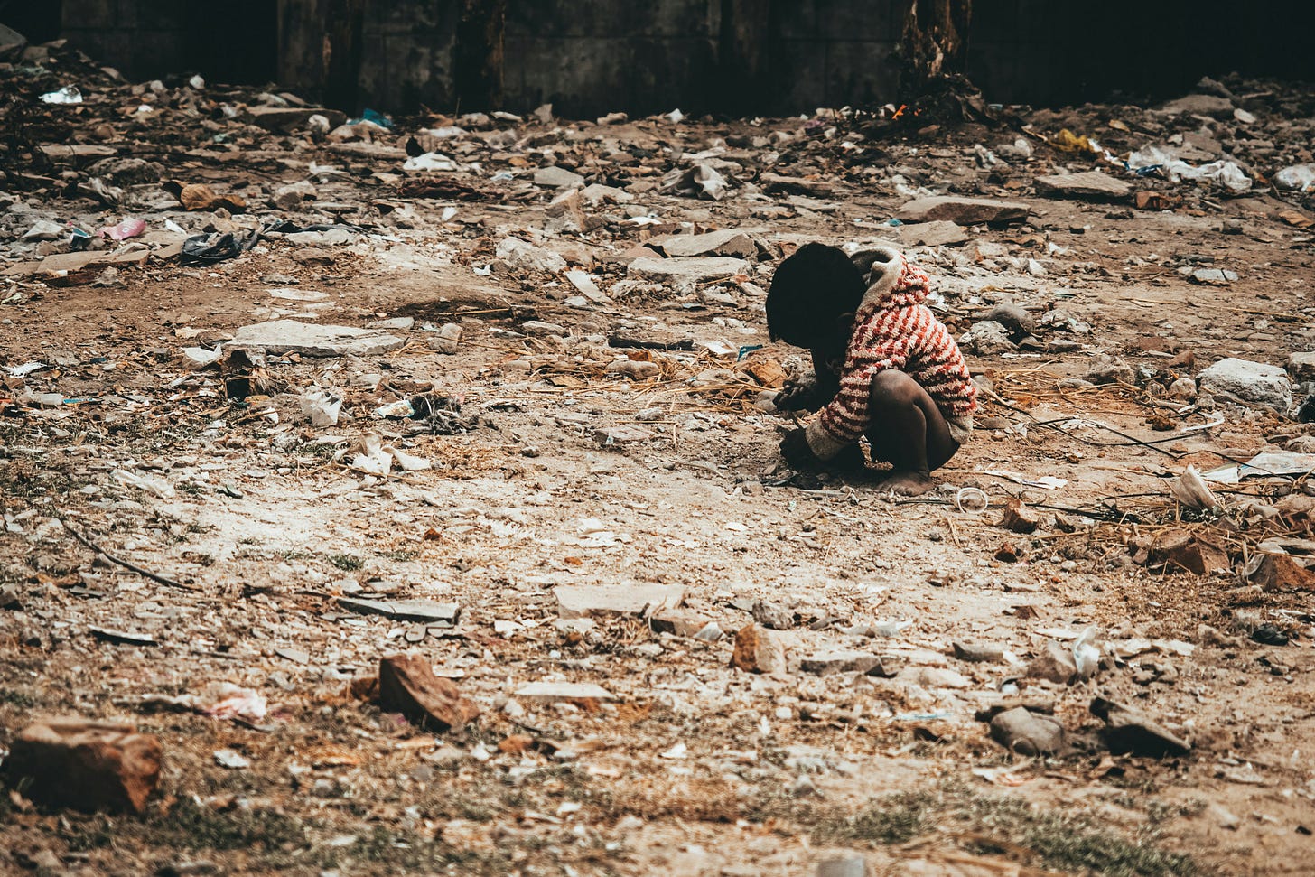 Child in striped clothing sits alone amid rubble and debris in conflict zone destruction Child in striped clothing sits alone amid rubble and debris in conflict zone destruction
