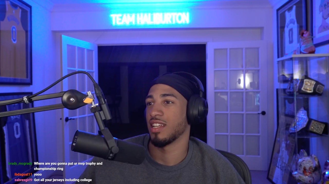 Pacers guard Tyrese Haliburton at his gaming setup, sitting in front of a microphone wearing a beanie and big headphones.