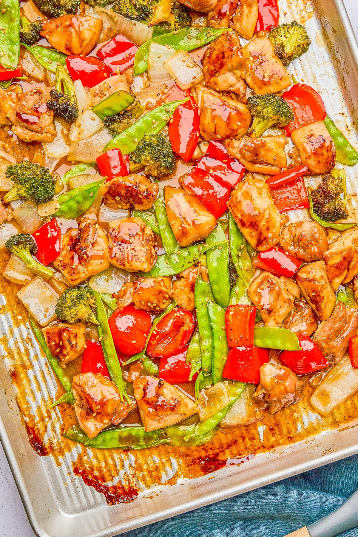 Sheet pan dish with glazed chicken pieces, red bell peppers, broccoli, snow peas, and onions.