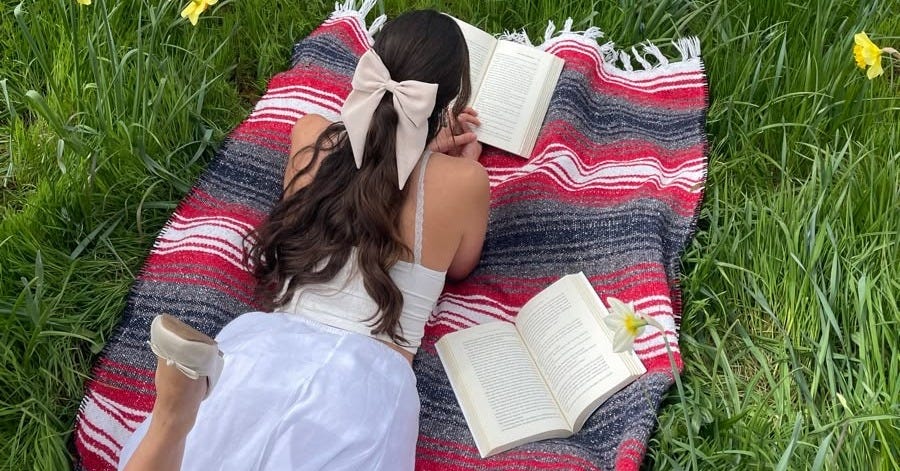 Woman reading a book outdoors in spring nature, representing mindfulness and creative rest for Substack writers