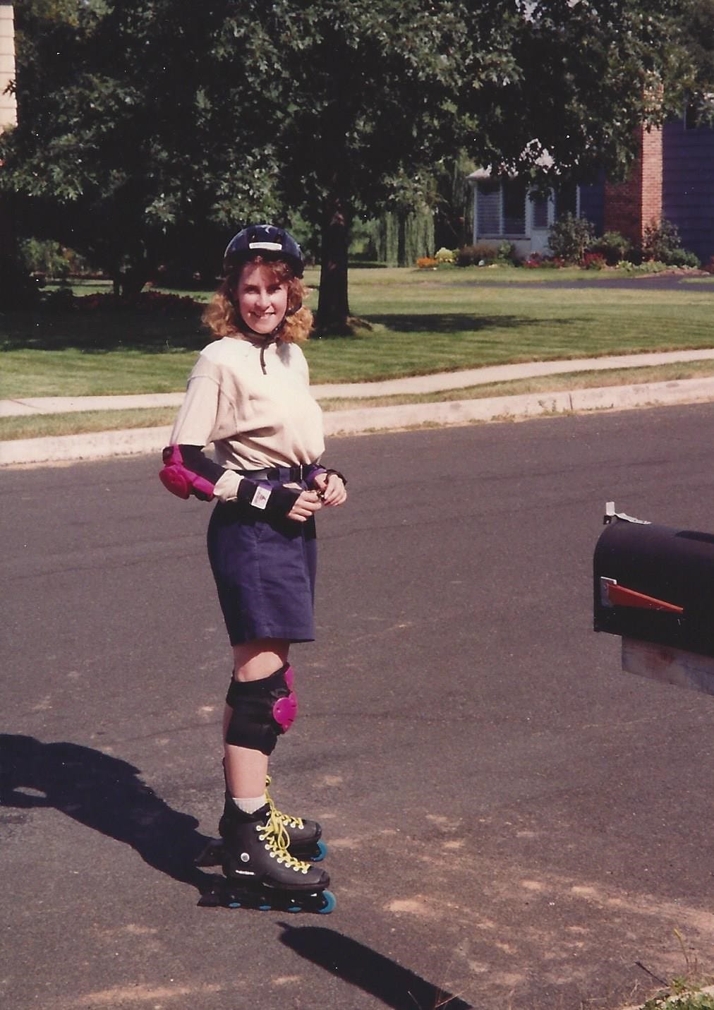 20-something woman wearing a helmet and elbow pads is suited up to rollerblade on a suburban street 20-something woman wearing a helmet and elbow pads is suited up to rollerblade on a suburban street