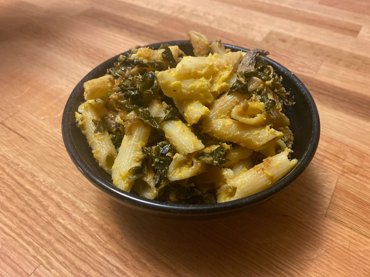 A ceramic bowl of full of penne with thick butternut squash sauce sits on a wooden counter.