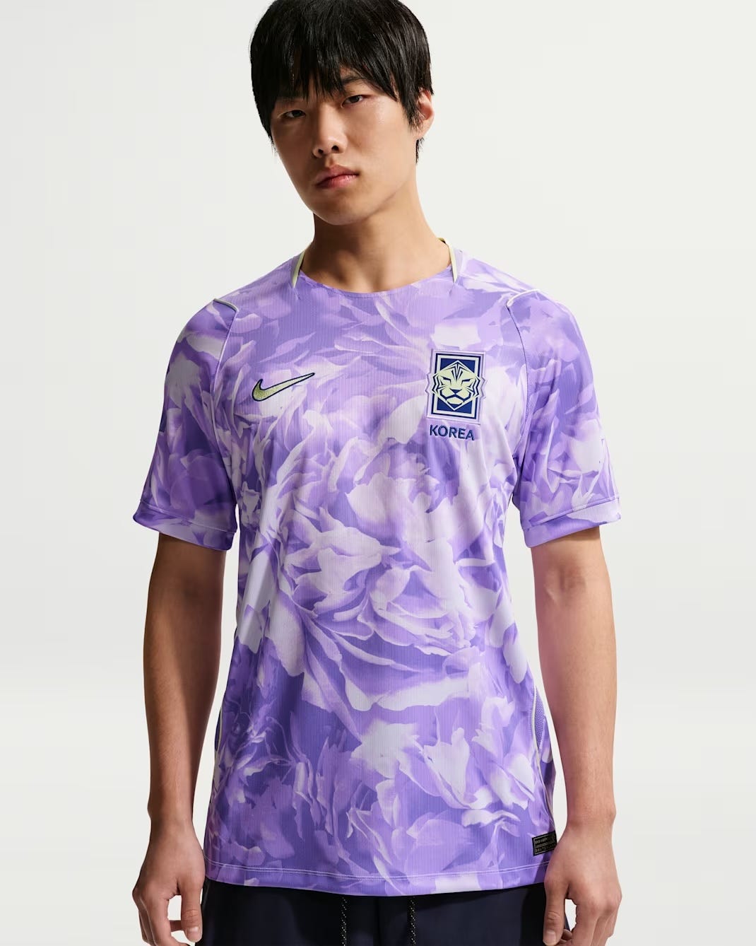 A model wearing South Korea’s 2026 Nike away jersey in a pale purple color with an all-over floral print, black shorts, and the South Korea crest on the chest.