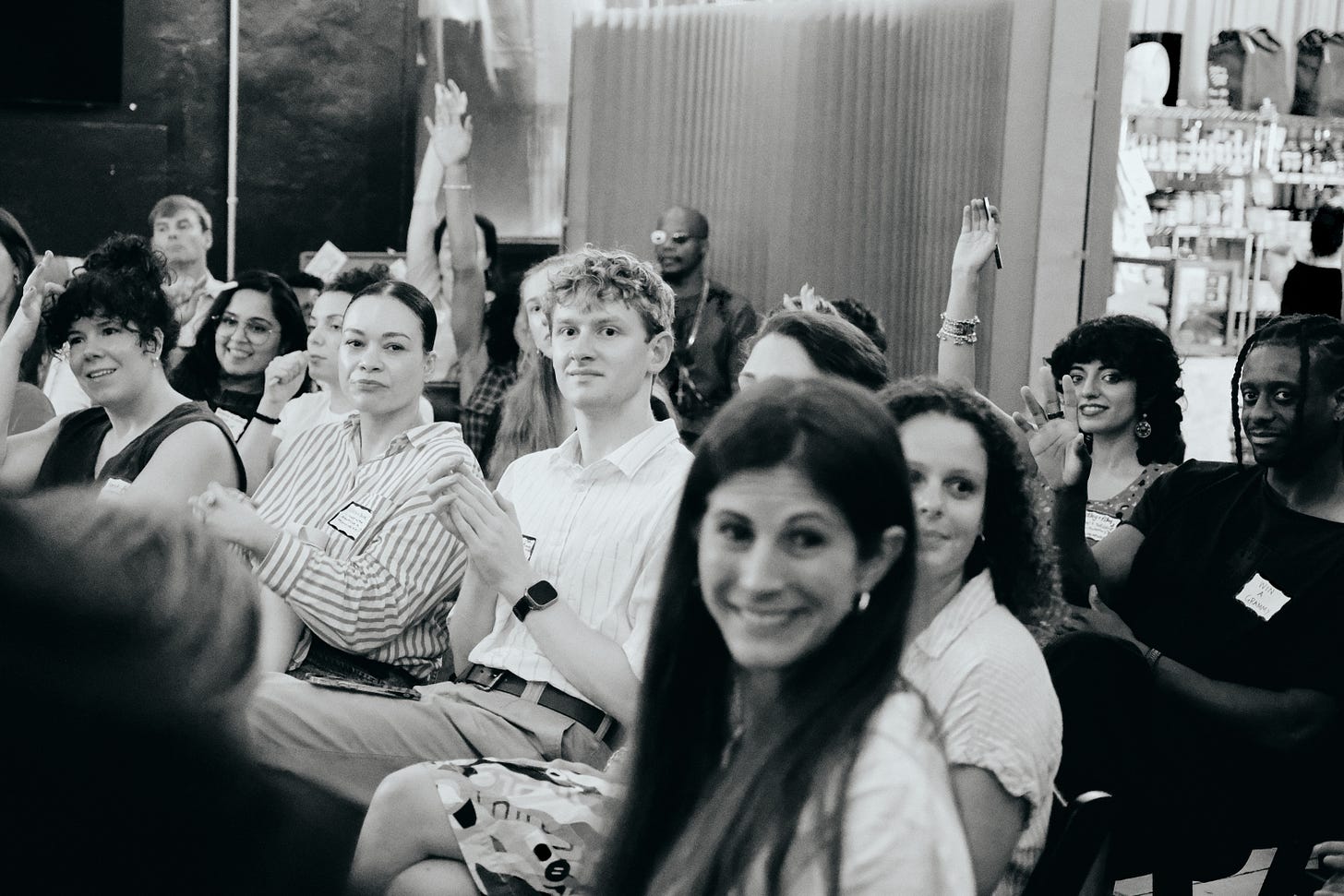 A dreamer smiles toward the camera as people wearing handwritten dream badges gather at Dreams & Obstacles NYC 1.