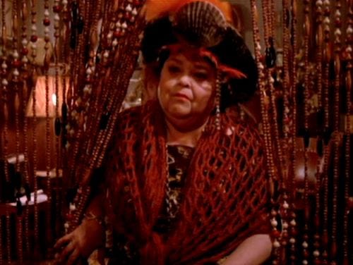 A witch wearing a had with a seashell and feathers parts beaded curtains to enter the room. A witch wearing a had with a seashell and feathers parts beaded curtains to enter the room.