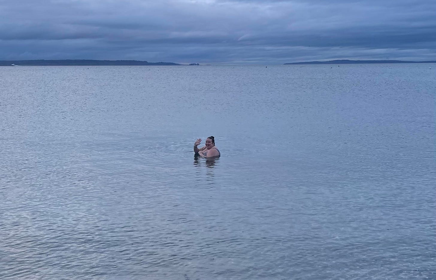 photo of Christina submerged in water up to her shoulders, outside in Puget Sound, waving to camera