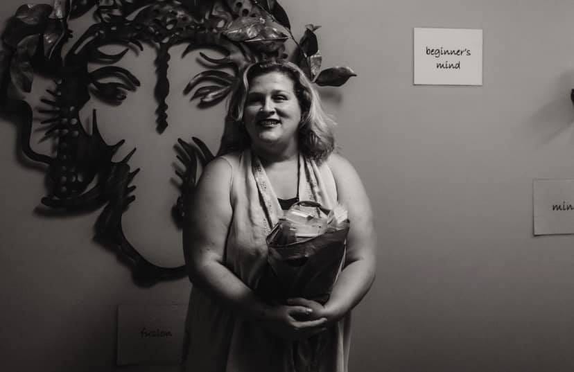 Picture of Jamie holding a bundle of papers in front of a metal wall hanging of Ganesh, the elephant god