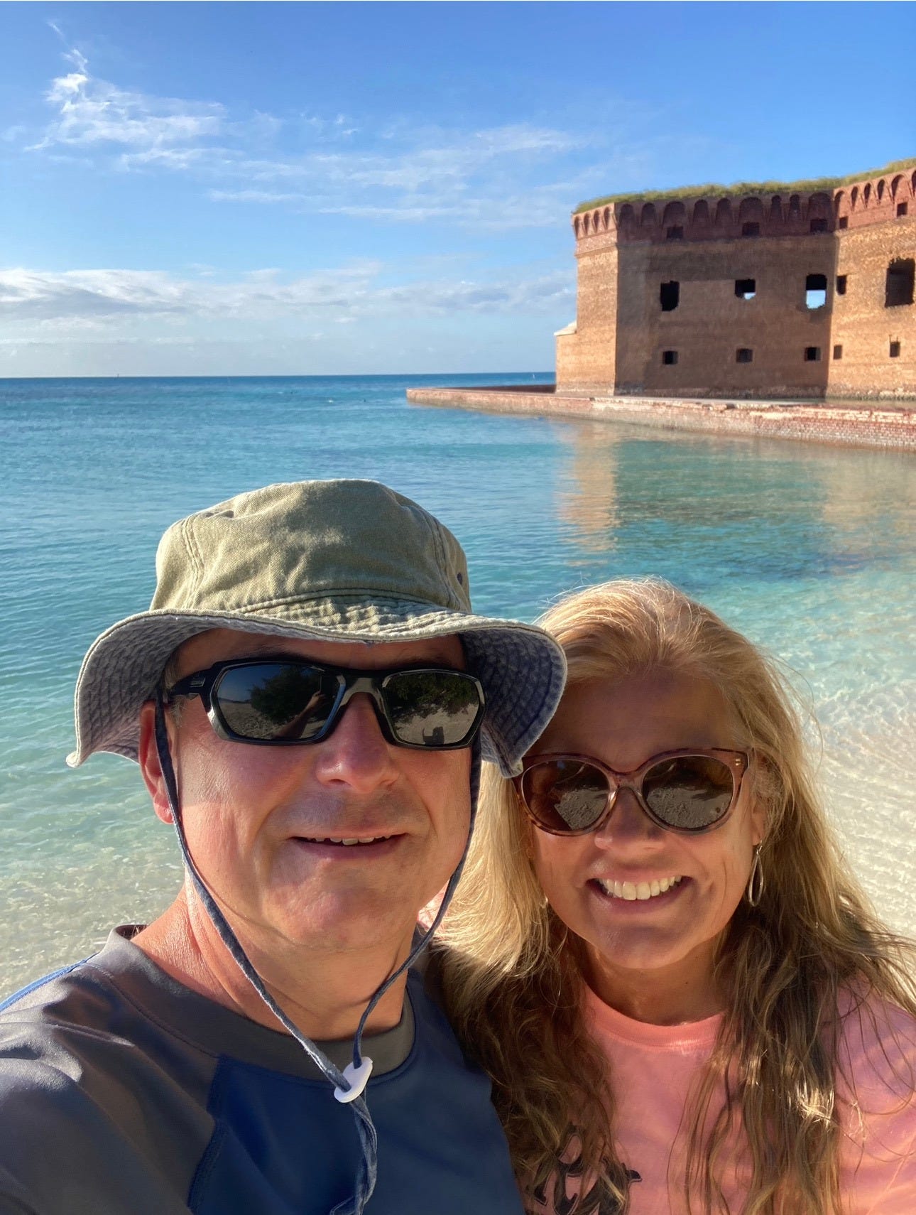 JP and his wife smiling in front of Fort Jefferson at Dry Tortugas National Park, with clear blue water and bright sky in the background.