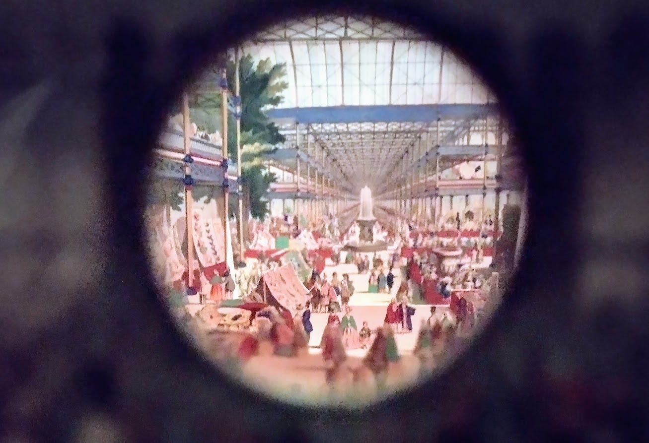 Round peepshow view of enormous glass building with tree, fountain, and two floors of exhibits around central atrium