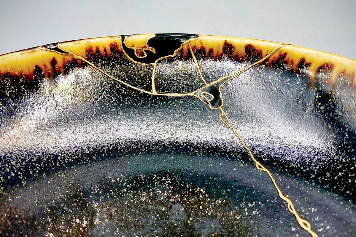 A black reactive crackle bowl featureing a golden repair technique called kintsugi.