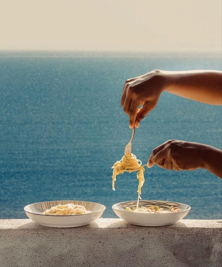 This may contain: two people are eating noodles off the edge of a cliff overlooking the ocean and blue water