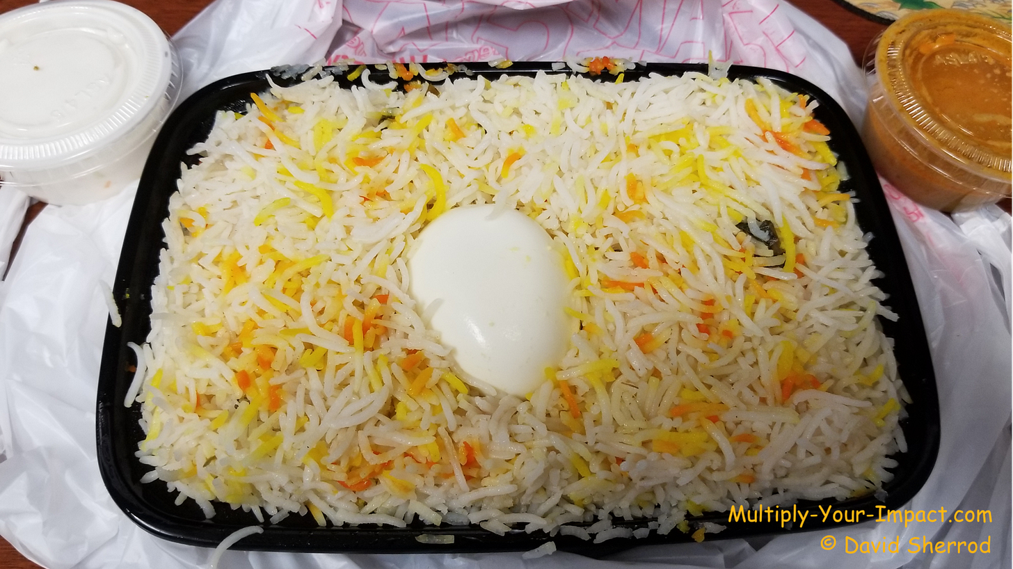 Takeaway meal of seasoned rice with what appears to be a hardboiled egg in the middle.