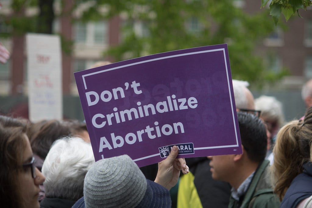 the photo is a close-up on a crowd of people in a parade. one of them is holding a purple sign from NARAL that says "don't criminalize abortion" and that is the center of the photo. you can't see anyone's faces or anything. You can see a brick building and a tree in the background. This photo was free on FLickr and was from the Seattle City Council so I assume the picture is from Seattle too