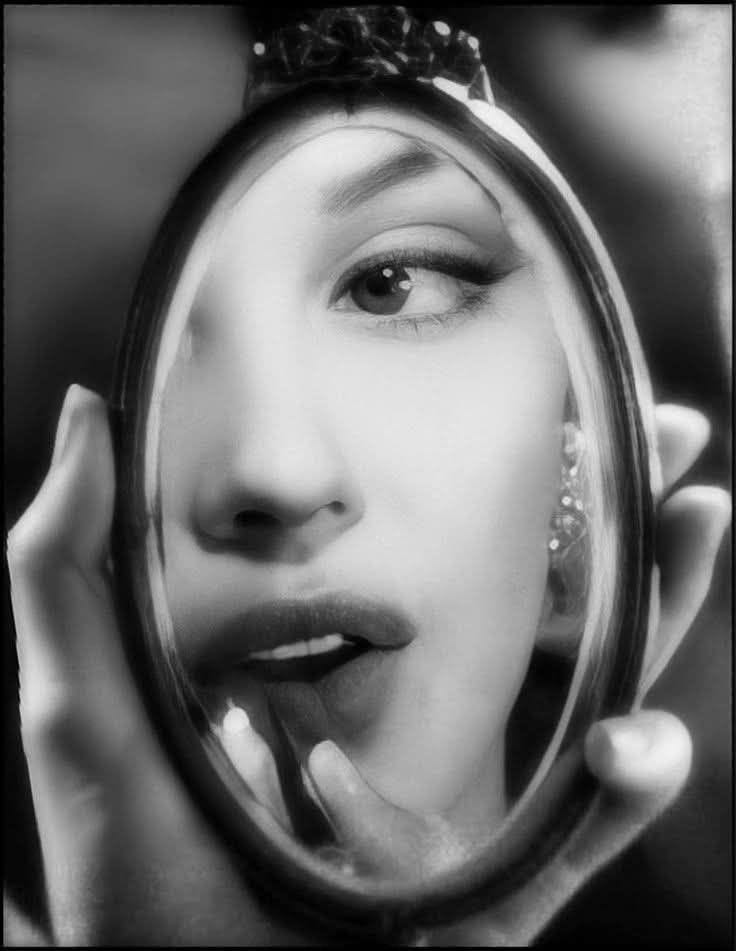 This may contain: a woman is looking into a mirror with her face reflected in it's reflection