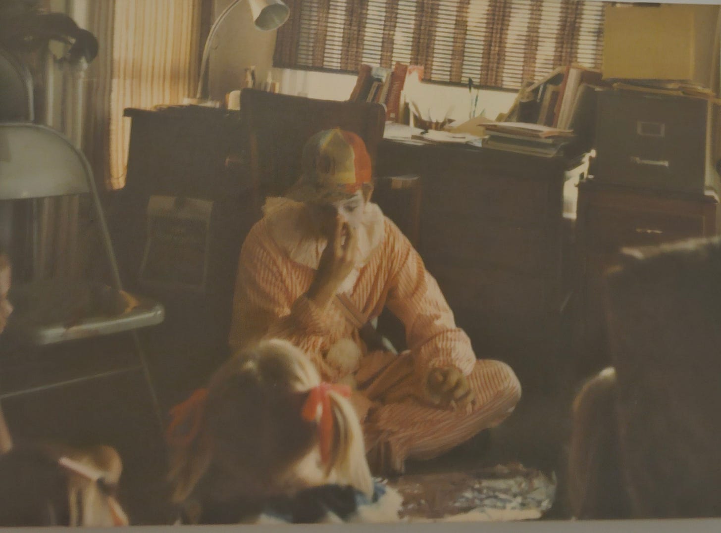 Grainy photo of a man dressed as a clown seated on the floor in front of a group of children. Grainy photo of a man dressed as a clown seated on the floor in front of a group of children.