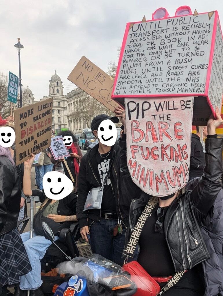 A disabled artist holding a cardboard dragon, surrounded by other protesters with cardboard signs. Text on the dragon says, Until public transport is reliably accessible without having to beg, or book in advance, or wait one year for the only lift to be repaired, or be turned away from a busy tube; until street curbs are level and roads are smooth, until the NHS can attend to chronic needs in a timely, focused manner… PIP will be the bare fucking minimum. A disabled artist holding a cardboard dragon, surrounded by other protesters with cardboard signs. Text on the dragon says, Until public transport is reliably accessible without having to beg, or book in advance, or wait one year for the only lift to be repaired, or be turned away from a busy tube; until street curbs are level and roads are smooth, until the NHS can attend to chronic needs in a timely, focused manner… PIP will be the bare fucking minimum.