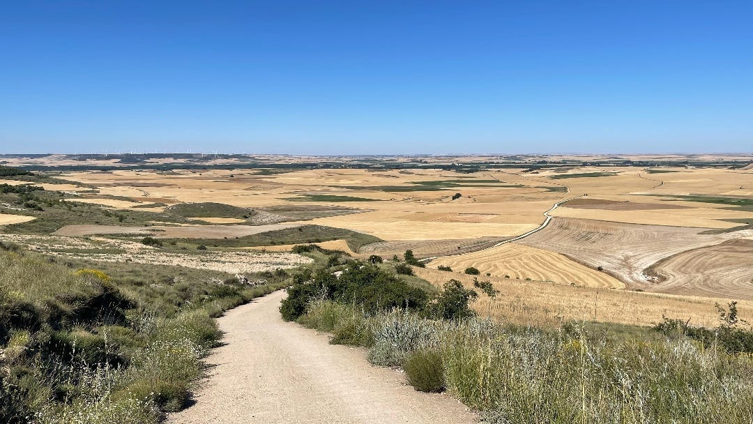 landscape as described: dry, light brown, a meandering path under a blue sky