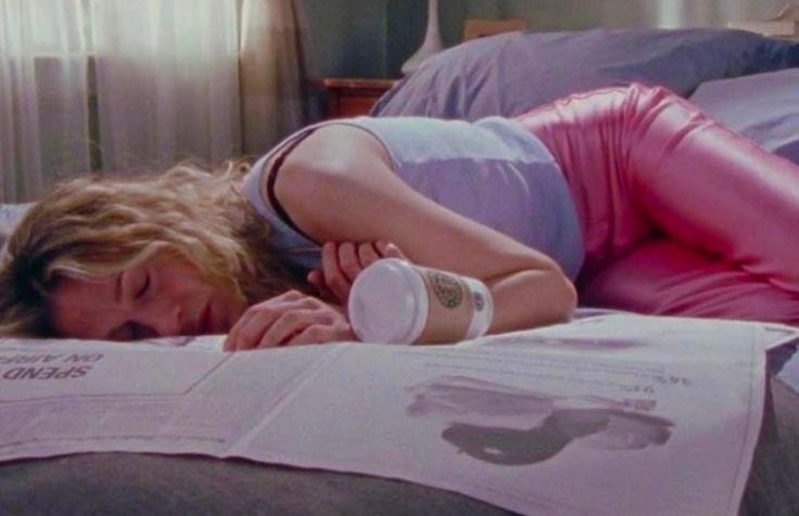 This may contain: a woman laying on top of a bed next to an open book and drinking from a cup