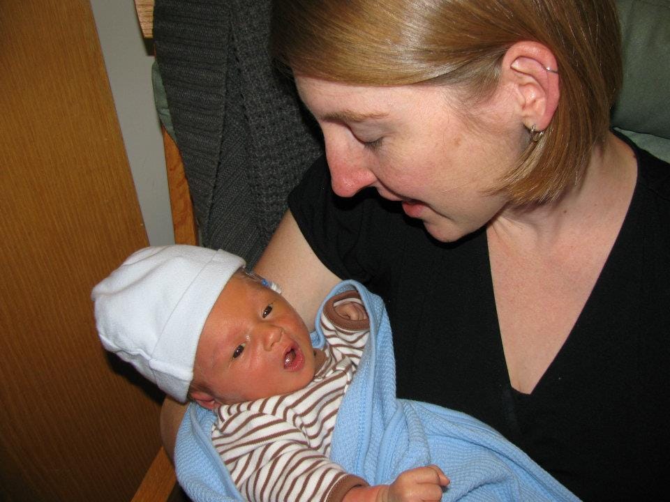 Mother holding her infant son who has an IV in his head barely visible under a newborn hat
