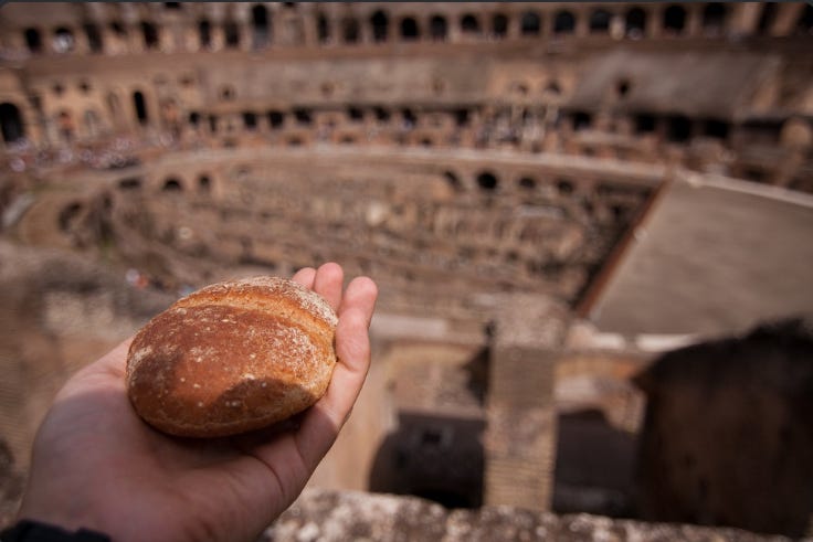 Hand holding bread roll in front of blurred out colloseum