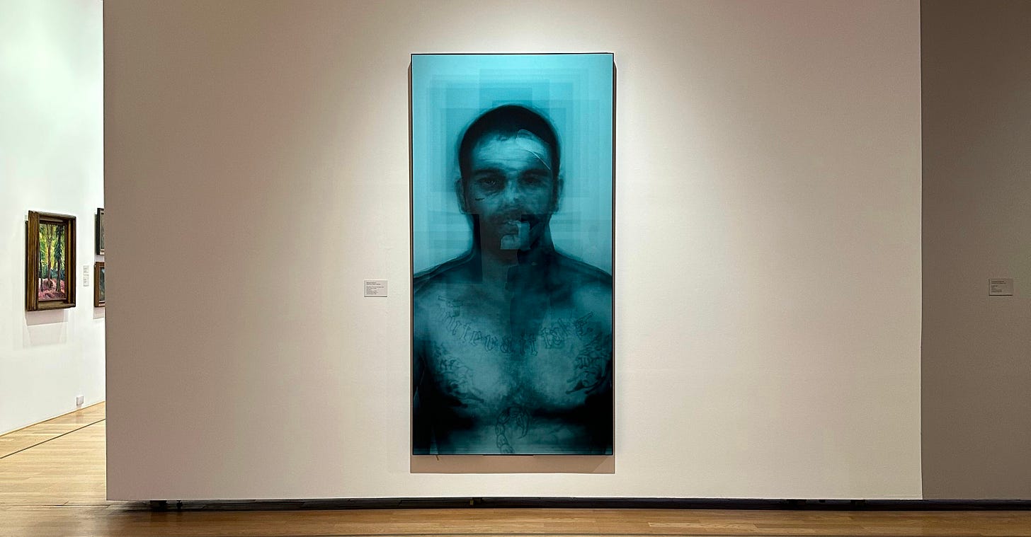 Obra “Guilty!” de Marcelo Grosman en el Museo Nacional de Bellas Artes: La imagen presenta una obra de arte colgada en una pared blanca de una galería. Se trata de un retrato ampliado y borroso de un hombre, visible principalmente desde los hombros hacia arriba. La imagen tiene un tono azulado y muestra características faciales distorsionadas, lo que le da un aspecto fantasmal y etéreo. El suelo de madera pulida refleja suavemente la luz del entorno de la galería, añadiendo un efecto calmante al espacio. Obra “Guilty!” de Marcelo Grosman en el Museo Nacional de Bellas Artes: La imagen presenta una obra de arte colgada en una pared blanca de una galería. Se trata de un retrato ampliado y borroso de un hombre, visible principalmente desde los hombros hacia arriba. La imagen tiene un tono azulado y muestra características faciales distorsionadas, lo que le da un aspecto fantasmal y etéreo. El suelo de madera pulida refleja suavemente la luz del entorno de la galería, añadiendo un efecto calmante al espacio.