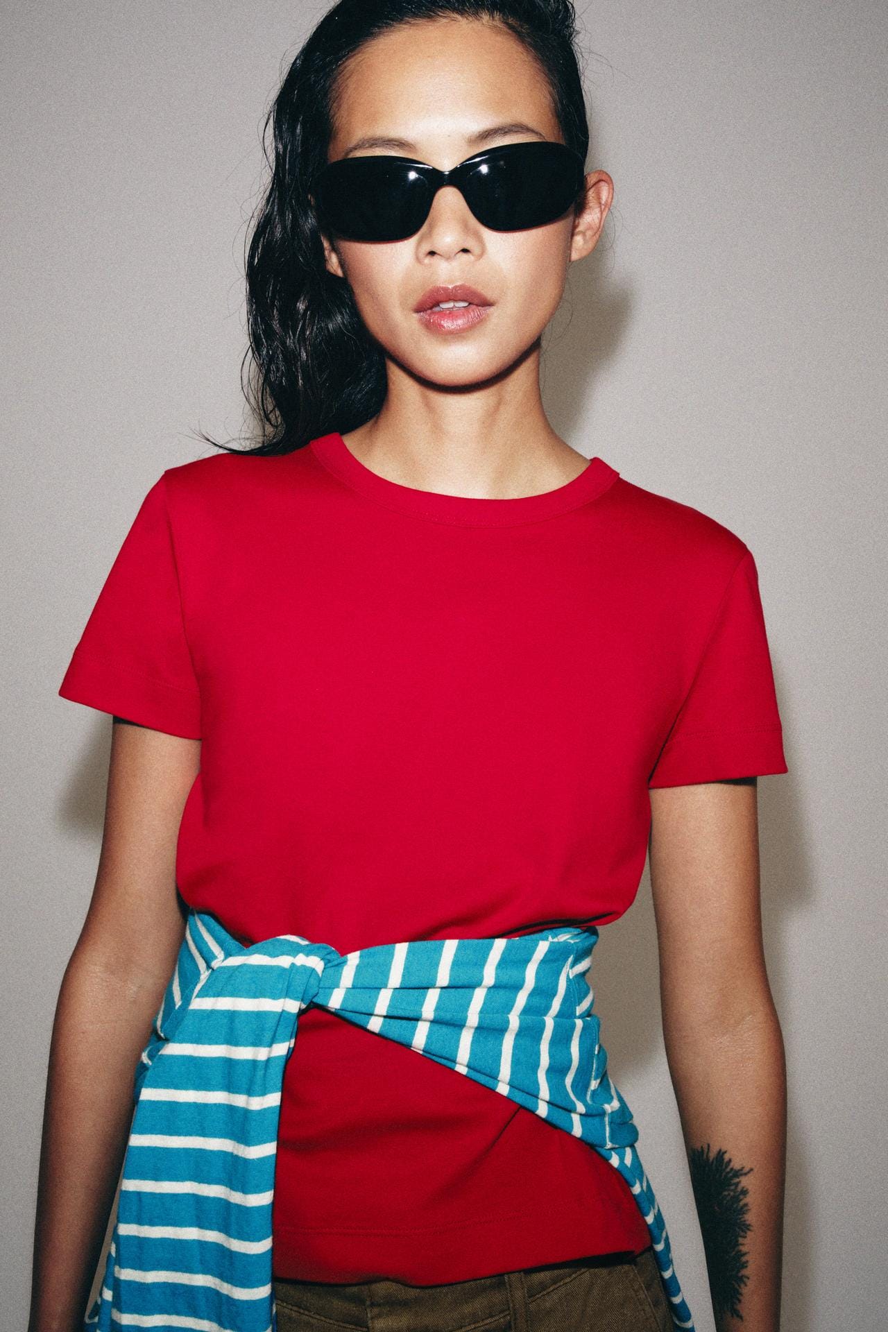 Medium shot of a plain red short-sleeved crew-neck t-shirt, with a blue and white striped shirt tied around the waist.