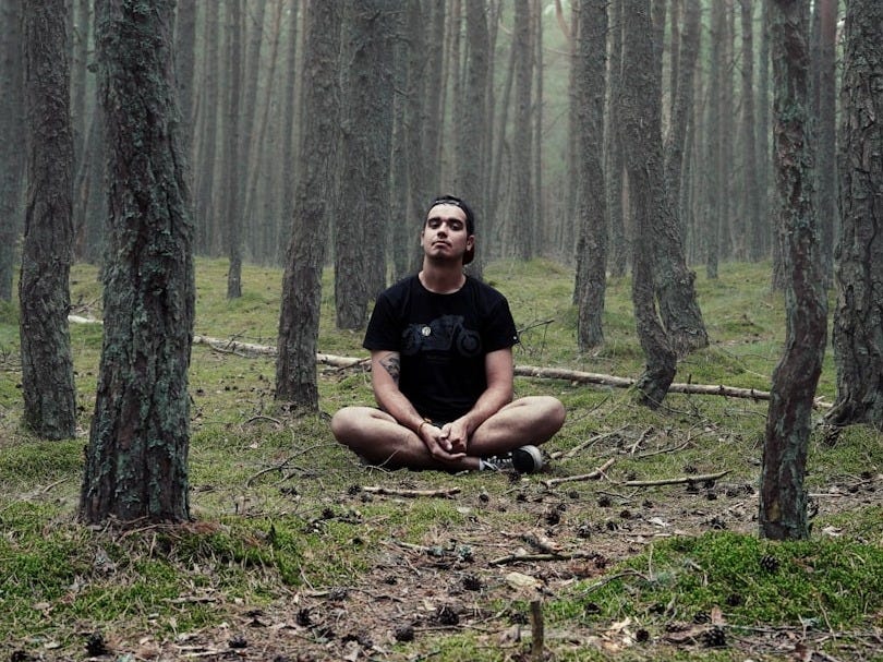 man in black shirt sitting in woods man in black shirt sitting in woods