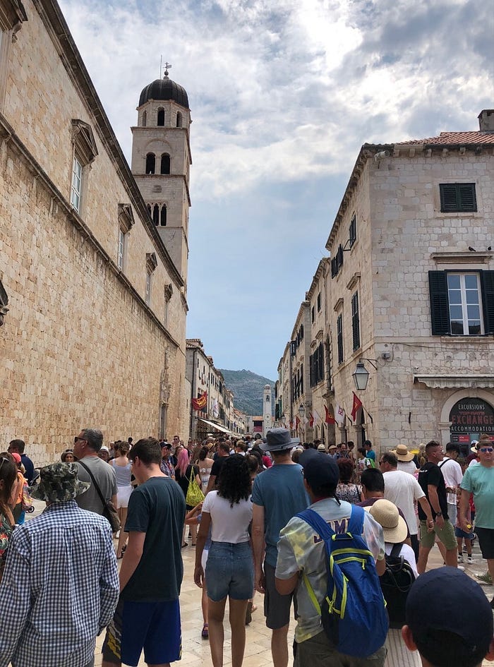 City street with stone buildings lining sides and crowds of tourists beneath.