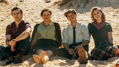 Four people sat side-by-side on sand dunes at the seaside. 