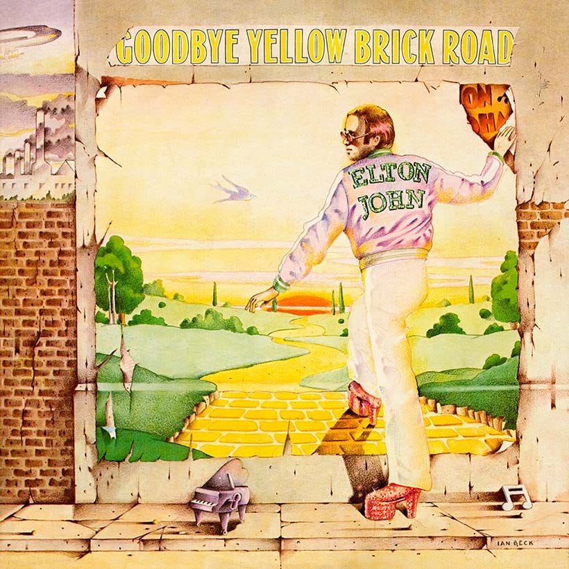An illustrated scene of a man in platform shoes stepping through a torn wall onto a winding yellow brick road that leads into a bright, fantastical landscape. He wears a pastel jacket with the words “ELTON JOHN” on the back. Above him, large yellow letters read “GOODBYE YELLOW BRICK ROAD.” A tiny purple piano sits on the ground in the foreground.