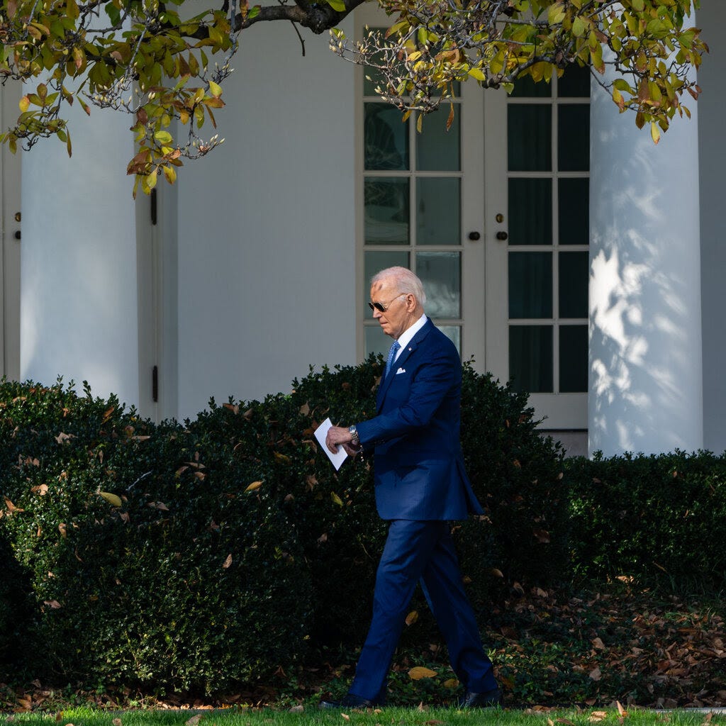 Joe Biden, as president, walks in the White House grounds carrying a slip of paper.