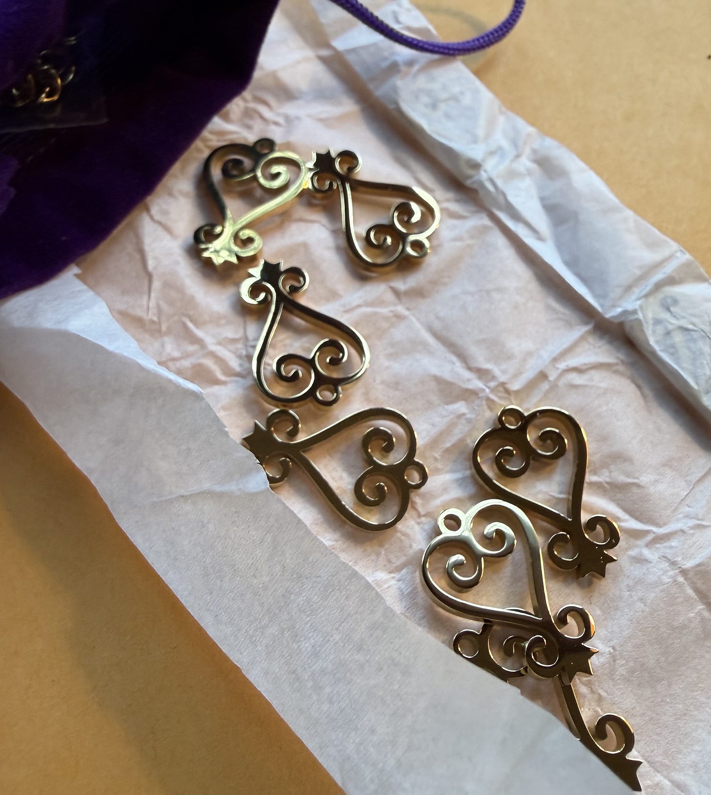 Gold metal sankofa symbol charms in white tissue paper Gold metal sankofa symbol charms in white tissue paper