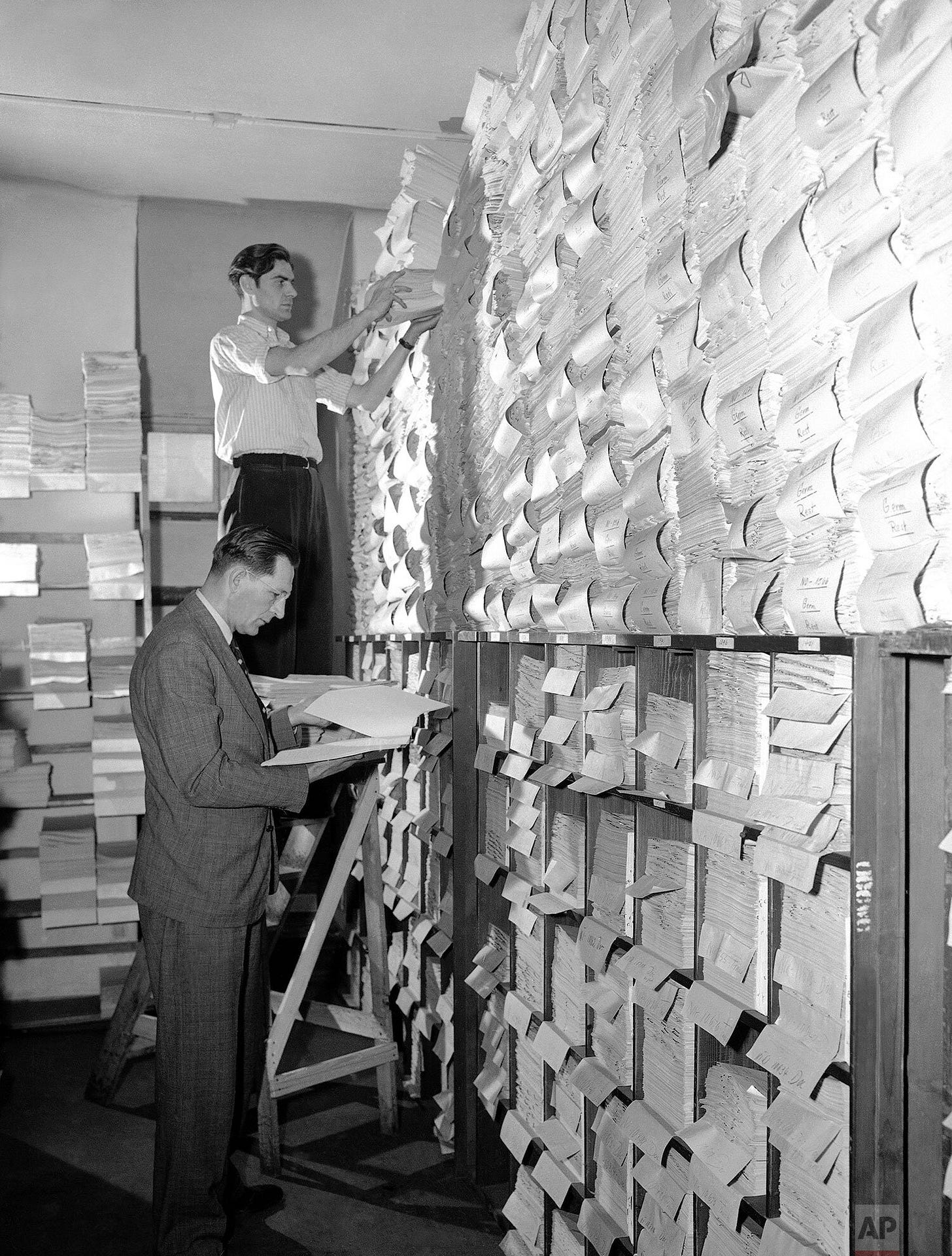 Fred Niebergall, Director of the Nuremberg Trials' document section, receives files from a German clerk in the document-filled Palace of Justice Building on June 16, 1948, highlighting the immense evidence gathered.