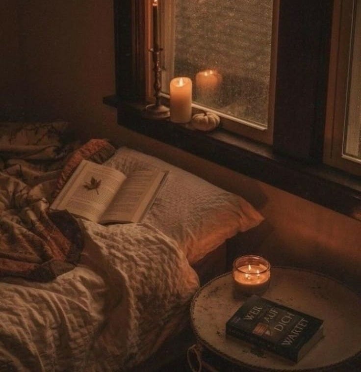 This may contain: an open book sitting on top of a bed next to a window with candles in it