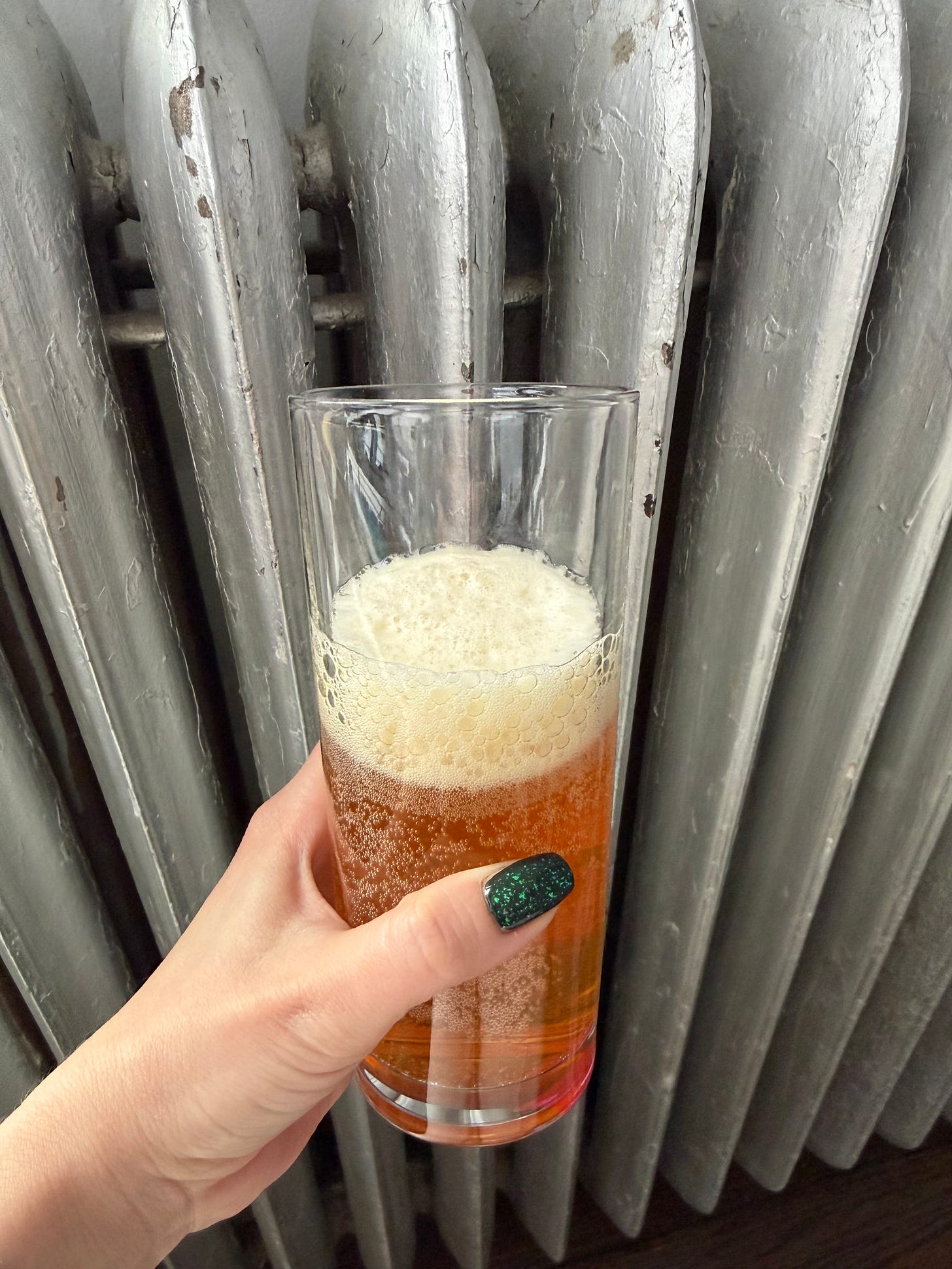 A glass of a dark orange carbonated liquid with foam A glass of a dark orange carbonated liquid with foam